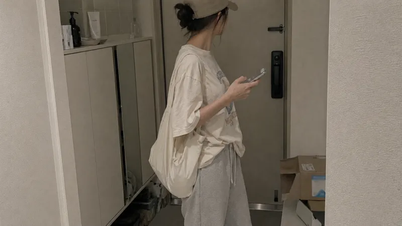 캡모자에 조거팬츠 입고 현관 나서며 스마트폰 확인하는 모습
